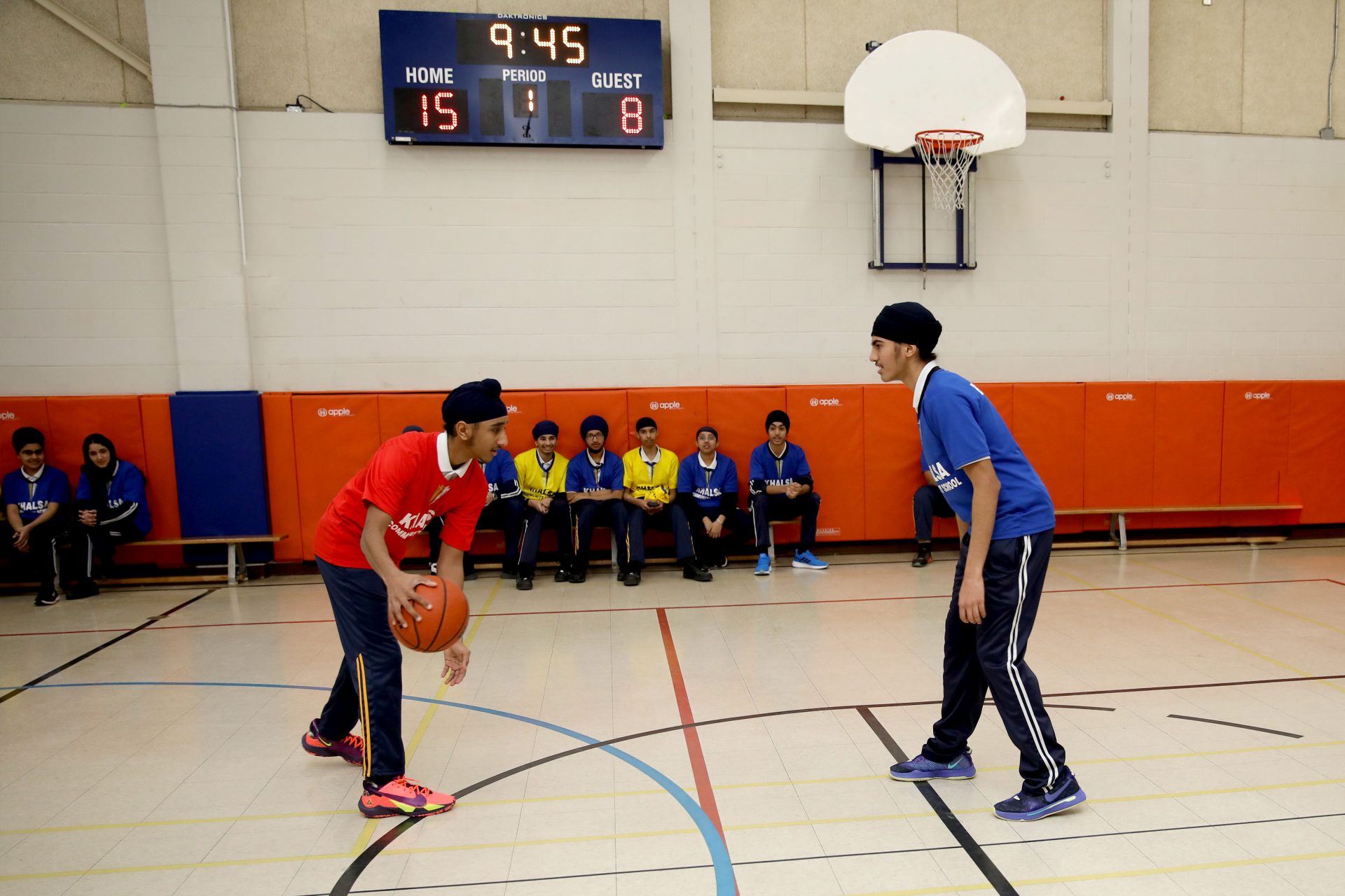 Students playing basketball in the school gymnasium while teammates watch from the bench