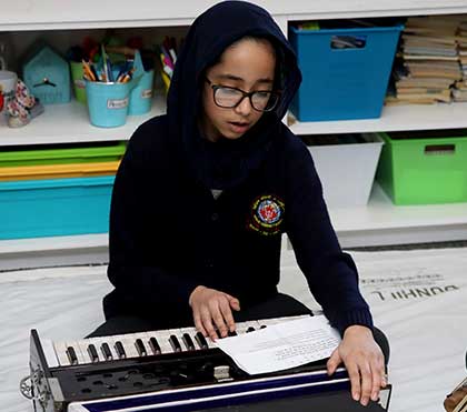 A student playing a harmonium from sheet music in a classroom